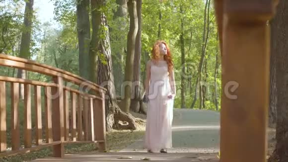 年轻的读头女孩在公园里散步漂亮的白种人女人穿着长而轻盈的裙子在阳光下休息视频的预览图