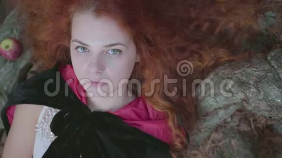 穿着黑色长袍的漂亮少女的特写镜头红色的衬里躺在树上看着摄像机可爱的年轻人视频的预览图