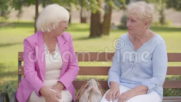 漂亮成熟的白种人女人坐在夏季公园的长凳上一头金发的老年妇女抱怨疼痛视频的预览图