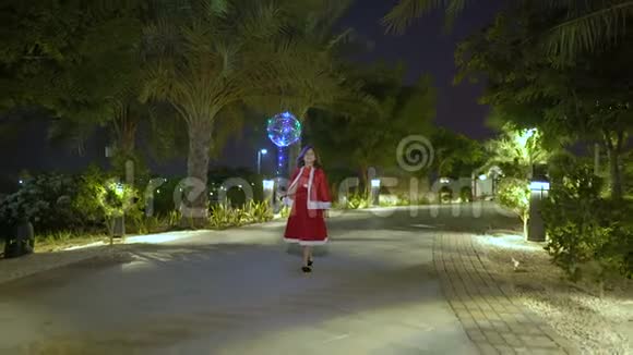 可爱的女孩准备庆祝圣诞节穿着红色圣诞老人衣服快乐的孩子走在棕榈树之间圣诞节时间视频的预览图