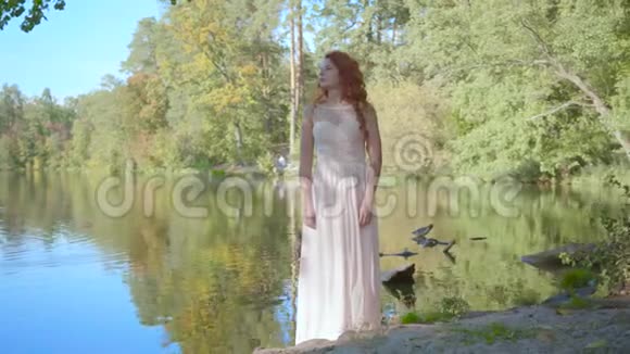 美丽的年轻白种人红色的头发穿着白色的长裙站在湖边漂亮的干脸视频的预览图