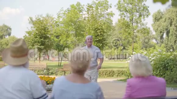 快乐的高加索老人在坐在长凳上的朋友们面前跳舞积极的老人娱乐成熟视频的预览图