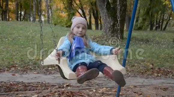 可爱的小女孩留着美丽的长发享受着秋风坐在花园里的木制秋千椅上视频的预览图