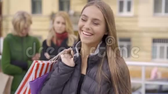 年轻的黑发女人长发开心地笑着看着相机快乐的白种人女孩站着购物袋视频的预览图