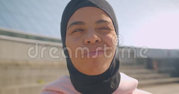 年轻迷人的戴头巾的非裔美国穆斯林女孩的特写照片看着镜头兴高采烈地笑着视频的预览图