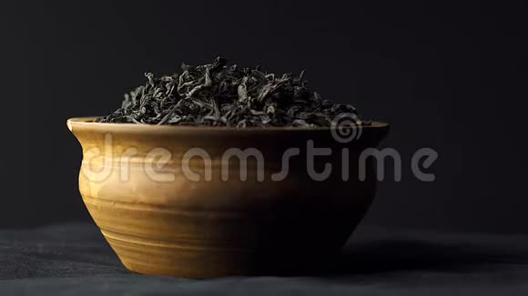 近景干红茶叶旋转在一个粘土碗在黑色背景概念中国传统茶视频的预览图