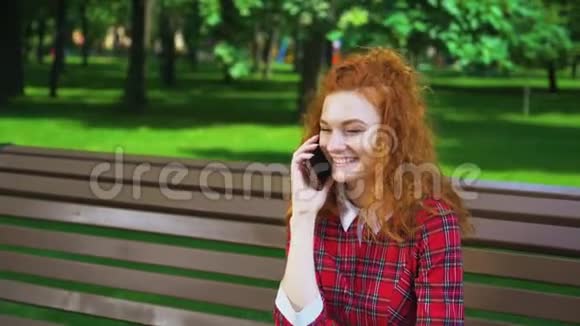 快乐的红发女孩在公园用手机和朋友聊天视频的预览图