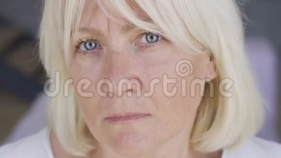 特写脸上一个害怕沮丧的成熟女人看着镜头家里有蓝眼睛和金发的女人视频的预览图