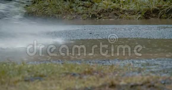 汽车轮胎在农村公路上的一个泥泞的泥坑里滚动和飞溅动作缓慢视频的预览图