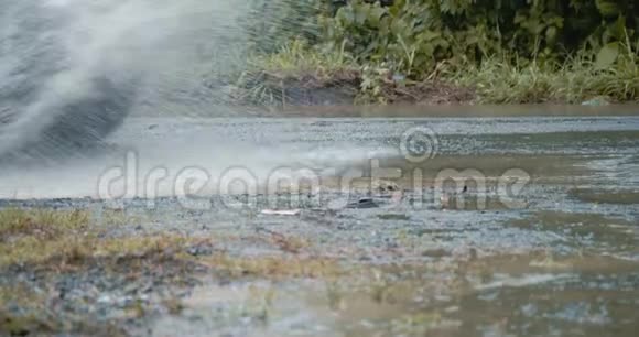 汽车轮胎在农村公路上的一个泥泞的泥坑里滚动和飞溅动作缓慢视频的预览图