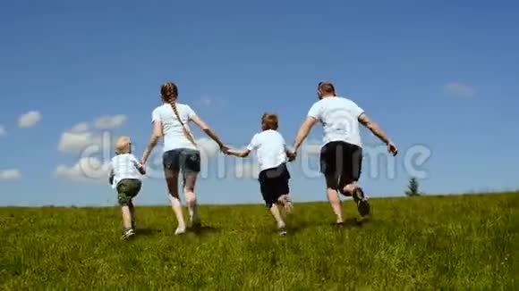 幸福的家庭母亲父亲和两个小儿子在一片绿色的草地上奔跑手牵着蓝天和云彩视频的预览图