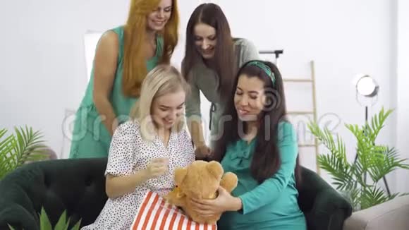 可爱的孕妇穿着蓝绿色丝绸连衣裙向她的朋友展示泰迪熊四个快乐的漂亮女孩视频的预览图
