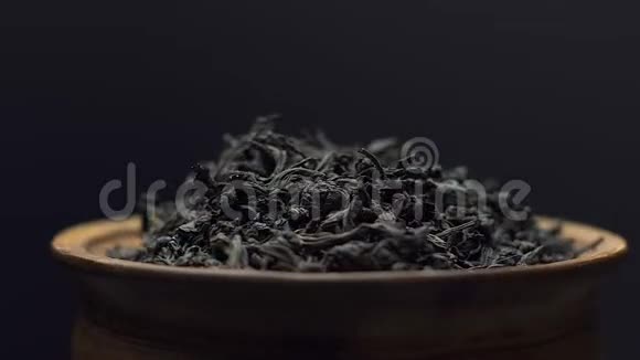 近景干红茶叶旋转在一个粘土碗在黑色背景概念中国传统茶视频的预览图