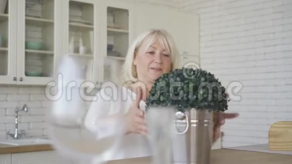 积极成熟的女人站在现代厨房里桶里有灌木一位照顾一个视频的预览图