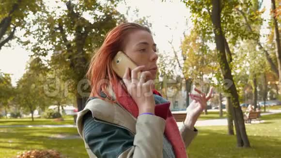 有着狐臭头发的女孩在公园里散步在电话里和一家网上商店的经理交谈在网上下订单视频的预览图