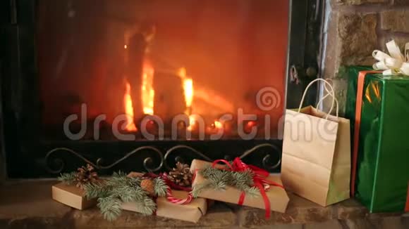 圣诞礼物装饰着云杉树枝球果丝带放在壁炉旁温暖的原木着火了圣诞节视频的预览图