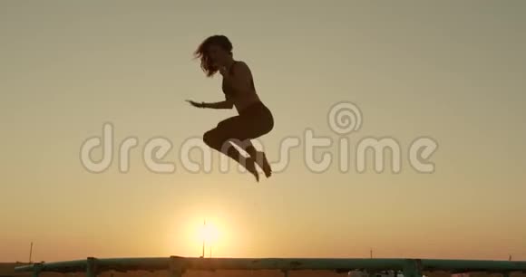 女孩在海滩上日落的阳光下跳上蹦床视频的预览图