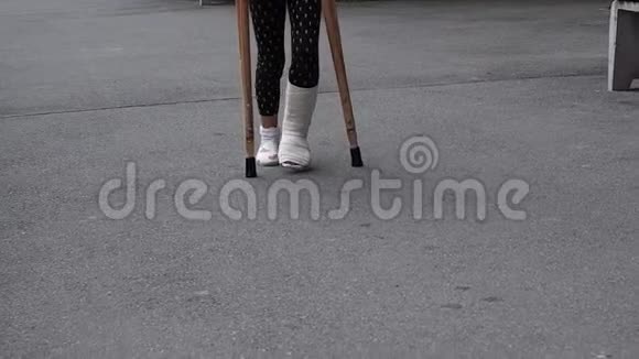 脚踝骨折的孩子拄着拐杖和石膏在街上行走踩在孩子们的脚上在户外散步一个视频的预览图