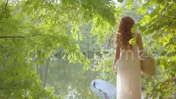 年轻的白种人女人穿着轻便的衣服穿过森林走到湖边穿白衣服的仙女视频的预览图