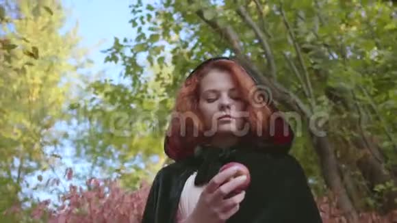 一个穿着黑色长袍的红发白种人女人的特写镜头看着她手中的苹果仙女站着视频的预览图