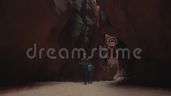 徒步旅行者在深洞斜坡峡谷中的沙质河床中带橙色红岩视频的预览图