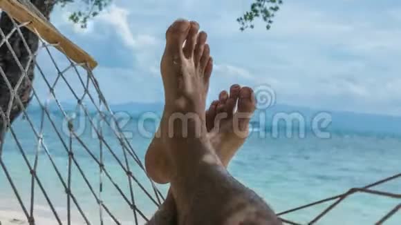 在蓝色的海洋前在度假的吊床上挥舞着赤裸的人脚和沙滩上的白沙视频的预览图