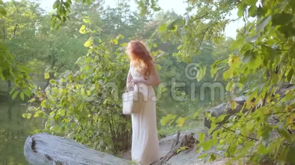 年轻优雅的白种人女孩穿着轻盈的长白色衣服站在河岸上的秋天森林里带着视频的预览图