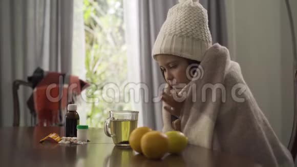 小女孩戴着冬帽戴着围巾在家里坐在餐桌旁喝茶视频的预览图