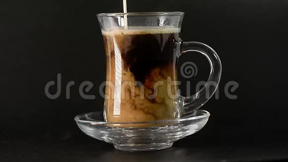 一滴牛奶倒进热气腾腾的咖啡里透明玻璃土耳其黑咖啡在黑暗中喝热饮料视频的预览图