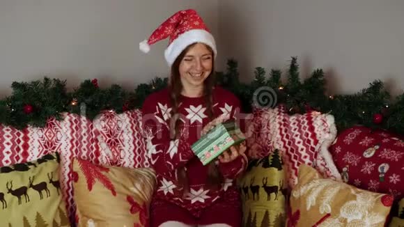 圣诞老人帽子里的女孩在看圣诞礼物盒打开它并感到快乐视频的预览图