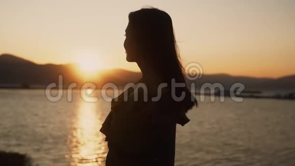 女人看着海滩上的日落张开双臂动作缓慢视频的预览图