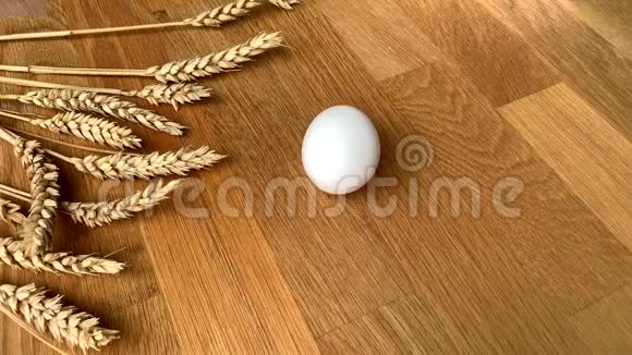 在成熟的麦穗背景下白鸡蛋在木桌上旋转复活节的概念视频的预览图