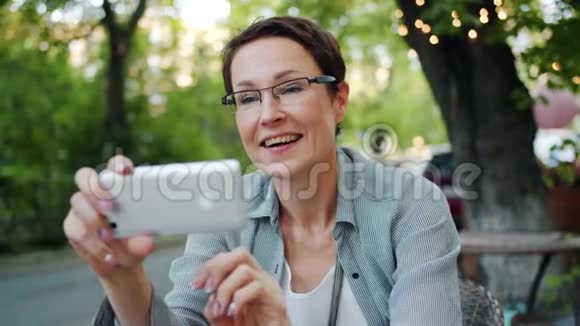 女性使用智能手机从户外咖啡厅进行在线视频通话的慢动作视频的预览图