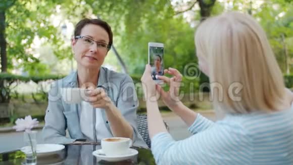 一位美丽的女士在街咖拿着一杯茶摆着智能手机摄像头视频的预览图