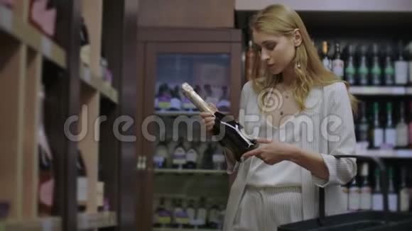 女孩在商店里买酒看瓶子上的标签在超市里选择酒精饮料视频的预览图
