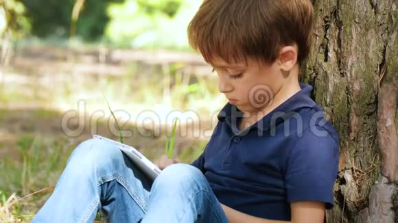 一个带平板电脑的小男孩的肖像快乐的孩子在大自然的背景下玩平板电脑视频的预览图
