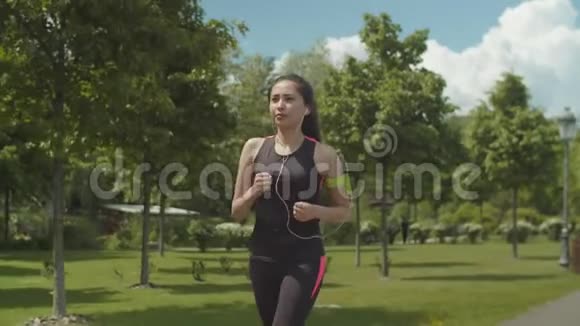 戴着耳机的女人在公园车道上奔跑视频的预览图