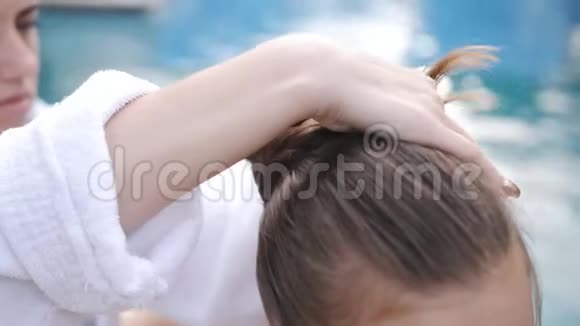 母亲和女儿坐在游泳池旁的休息室里母亲梳女儿头发视频的预览图