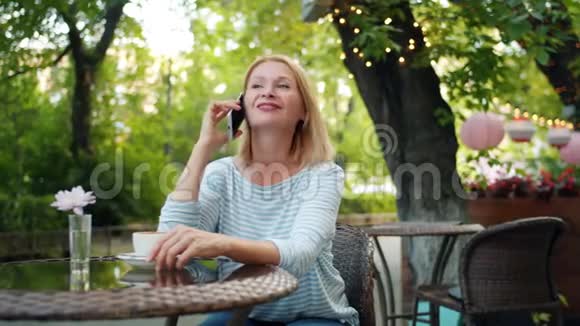 快乐的成熟女人在手机上笑着坐在街边咖啡馆视频的预览图