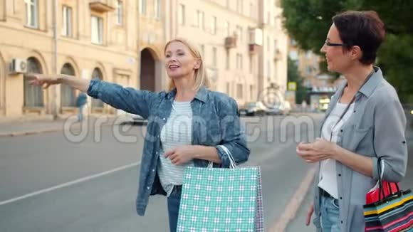 微笑的女人带着购物袋在城市街道上挥舞着出租车视频的预览图