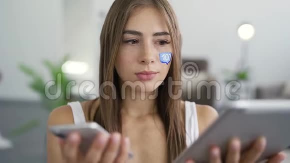 年轻貌美的女人的肖像脸上画着留言盒手里拿着电话和平板电脑微笑着视频的预览图
