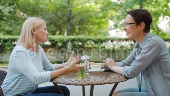 成熟的女士在露天咖啡馆和朋友聊天在餐桌上开怀大笑视频的预览图
