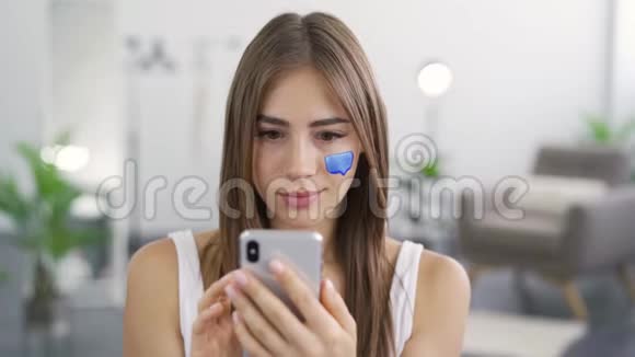 坐在家里用手机发短信的年轻可爱女人的特写镜头女孩脸上画的留言框视频的预览图