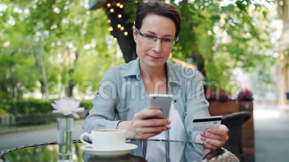 在街头咖啡馆女士用智能手机支付信用卡的动作缓慢视频的预览图