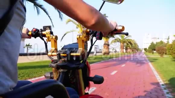 在度假小镇上女人骑着一辆电动滑板车在一条红色的自行车道上骑着棕榈树视频的预览图