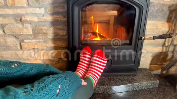 女人坐在炽热燃烧的壁炉旁双臂双腿张开穿着红袜子走向炉火冬季放松的理念视频的预览图
