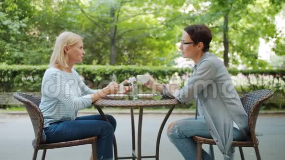 美丽的中年妇女在户外咖啡馆里捧着咖啡杯聊天视频的预览图