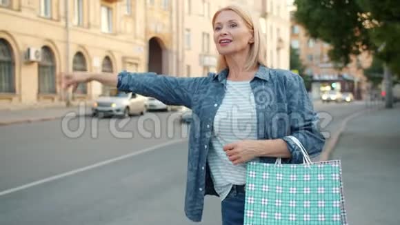 成熟的女人带着购物袋微笑着向出租车挥手视频的预览图