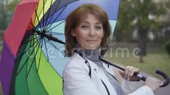自信的白种人女人旋转着多种颜色的伞微笑着快乐的成年女性站在阳光明媚的夏天视频的预览图
