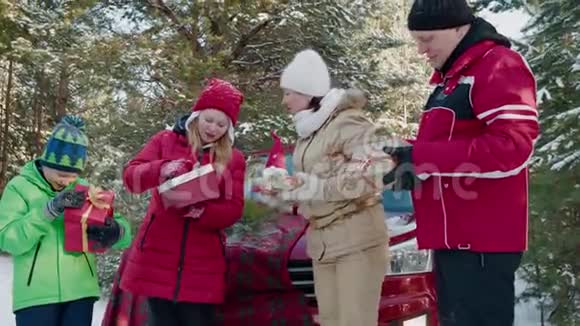 冬天散步时一家人在雪地森林里检查新年礼物带圣诞礼物的快乐女儿打开盒子视频的预览图